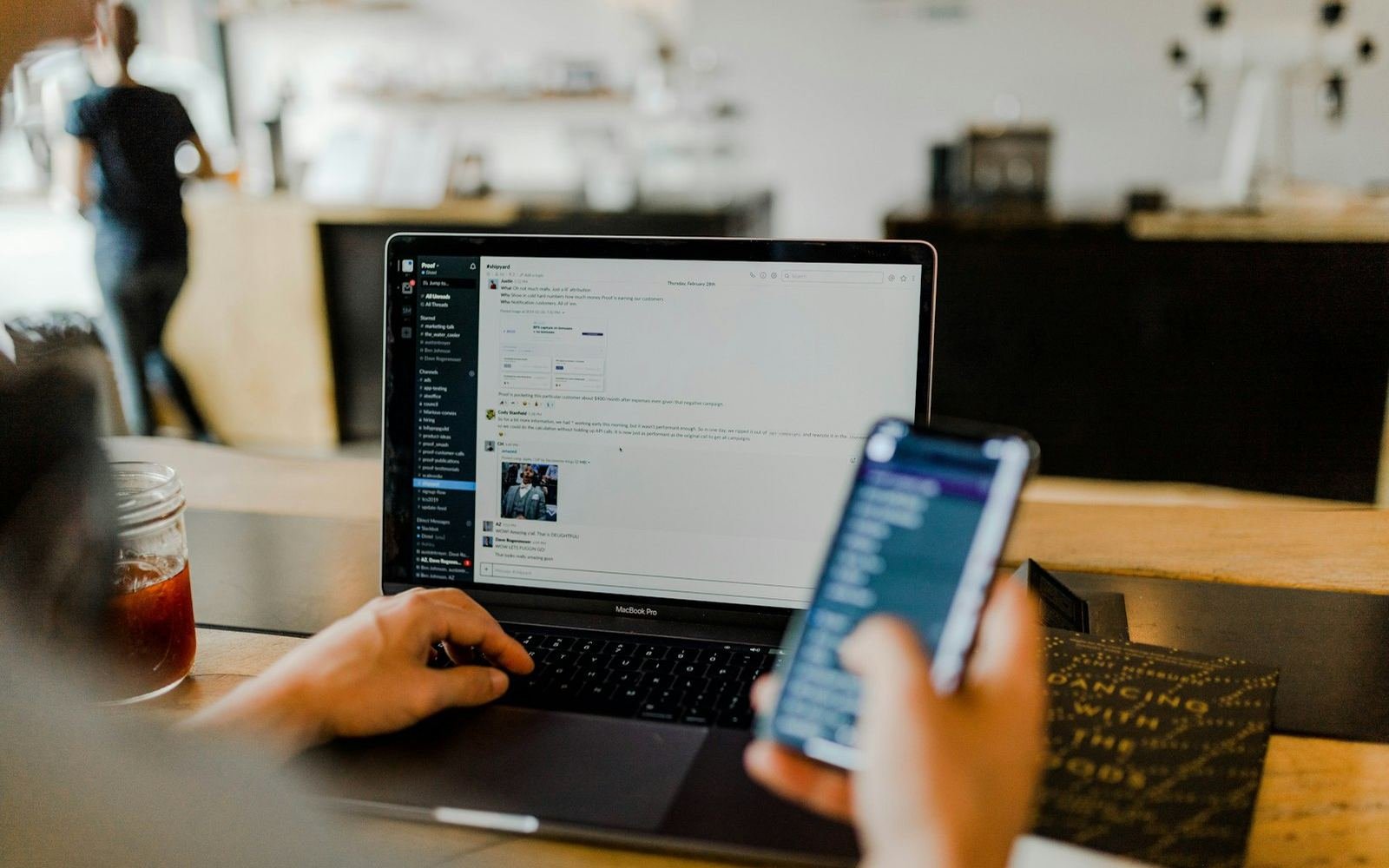 Person using a phone and laptop together at a cafe table
